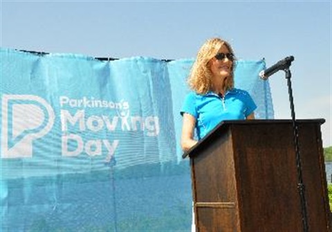 Woman standing at podium in front of blue curtain with text 